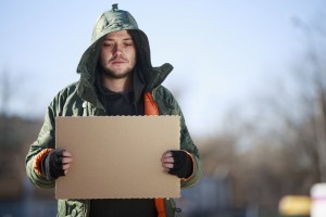 Homeless person with blanck cardboard. Focused on cardboard