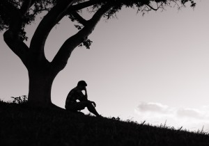 Sad young men sitting under tree in the park.